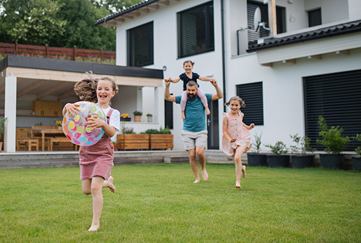 Vater mit drei Töchtern, die draußen im Hinterhof spielen und laufen.